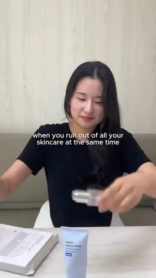 A woman at a table holds up a skincare bottle. On-screen text reads: when you run out of all your skincare at the same time.